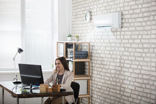 Climatisation Maurepas - femme qui regarde son ordinateur en dessous d'un climatiseur au plafond