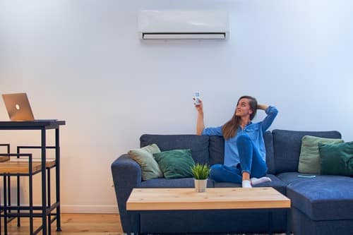 Climatisation Morangis  - femme qui tient une télécommande pour régler un climatiseur au dessus d'elle