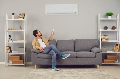 Climatisation Vaureal - homme assis sur un canapé qui tient une télécommande pour régler un climatiseur mural
