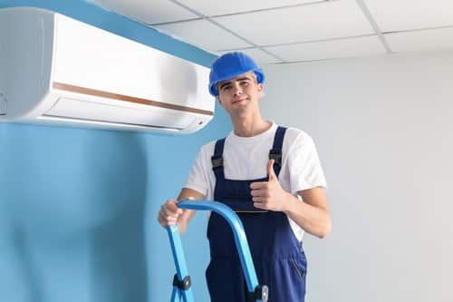 Climatisation Beauzelle - homme qui est sur une échelle pour régler un climatiseur au plafond devant un mur bleu