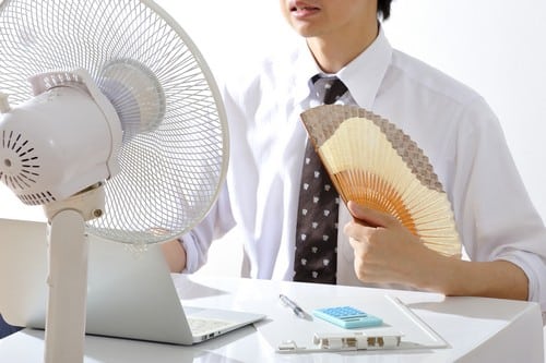 Climatisation Caudry - homme assis sur un bureau devant un climatiseur