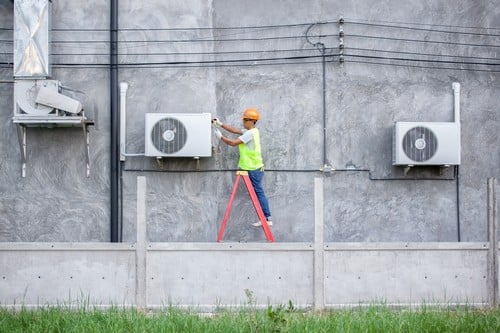 Climatisation Cavaillon - homme sur une échelle qui règle un climatiseur sur un mur en extérieur