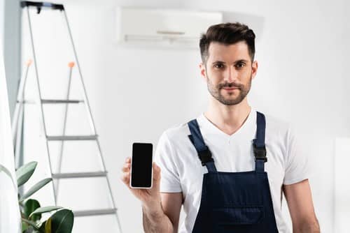 Climatisation Faches-Thumesnil - homme qui tient un téléphone pour régler un climatiseur au plafond derrière lui