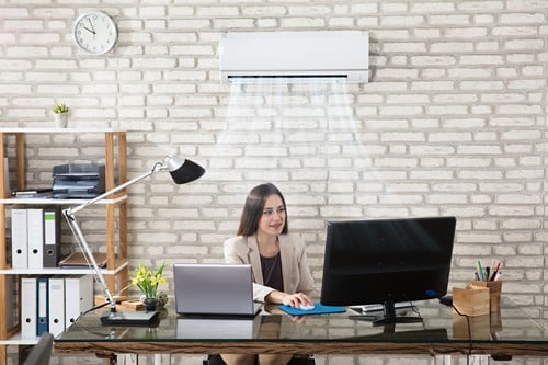 Climatisation Raismes - femme assise à son bureau en dessous d'un climatiseur