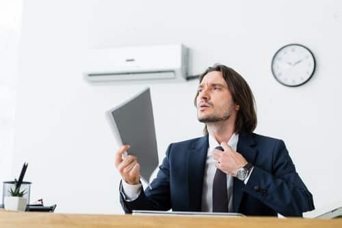 Climatisation Saint-Loubes - homme assis à son bureau en dessous d'un climatiseur